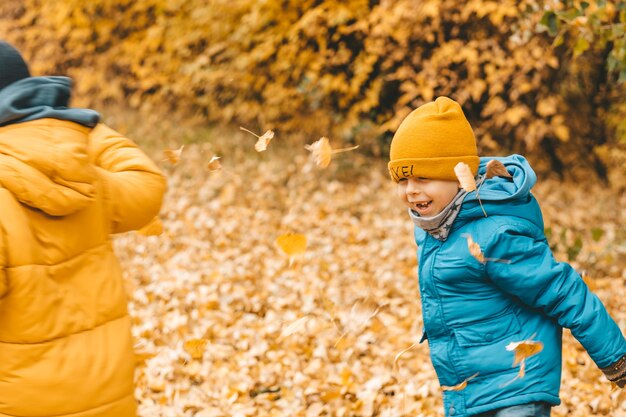Meninos com uma jaqueta espalham folhas em um parque de outono. A criança se alegra com as folhas de outono. Os meninos estão felizes com o outono. Caminhando no parque outono. Infância feliz