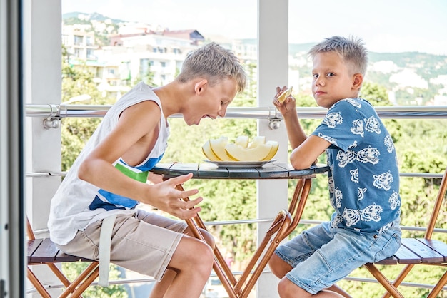 Meninos da escola gostam de comer melão fresco no terraço do hotel com expressão animada