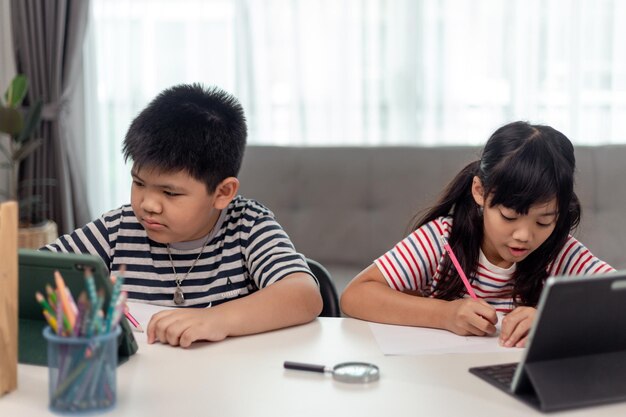 Meninos e meninas asiáticos gostam de aprender online fazendo anotações e usando tablets em casa