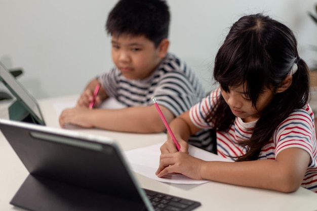 Meninos e meninas asiáticos gostam de aprender online fazendo anotações e usando tablets em casa