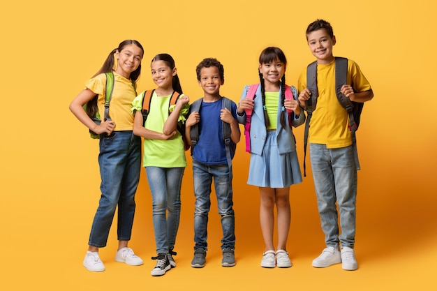 Meninos e meninas felizes posando com mochilas posando em amarelo