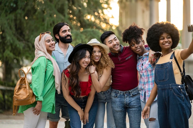 Meninos e meninas multiétnicos tirando selfie ao ar livre com luz de fundo Conceito de amizade de estilo de vida feliz sobre jovens multiculturais se divertindo juntos na cidade