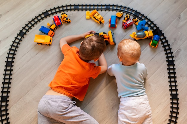 Meninos em idade pré-escolar desenhando no chão no papel, brincando com brinquedos educativos - blocos, trem, ferrovia, veículos em casa ou creche. brinquedos para pré-escola e jardim de infância. vista do topo.