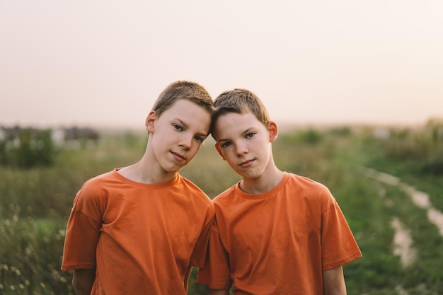 Meninos gêmeos engraçados em camiseta laranja brincando ao ar livre no campo ao pôr do sol Estilo de vida de crianças felizes