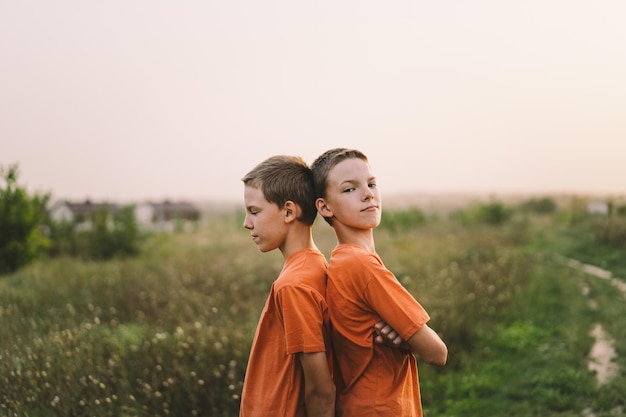 Meninos gêmeos engraçados em camiseta laranja brincando ao ar livre no campo ao pôr do sol Estilo de vida de crianças felizes