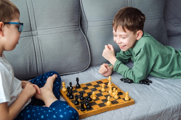 Meninos jogam xadrez de madeira deitado em um sofá cinza