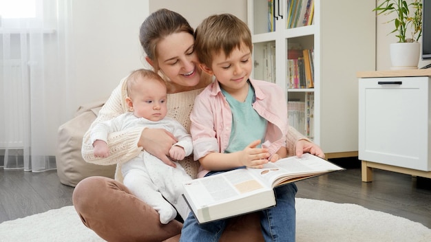 Foto meninos sorridentes com uma jovem mãe lendo um livro de contos de fadas na sala de estar de casa