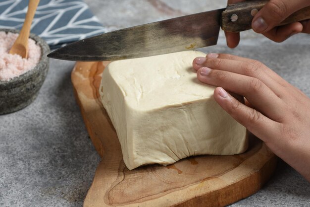 Menns manos cortando tofu blanco sobre tabla de madera