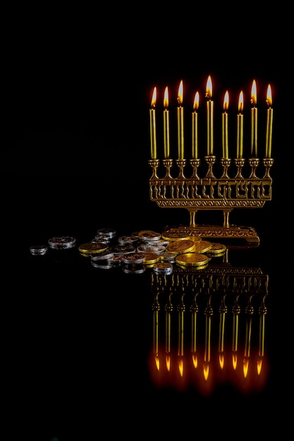 Menorá com velas douradas, moedas de chocolate e reflexo na superfície para o feriado judaico de Hanukkah.