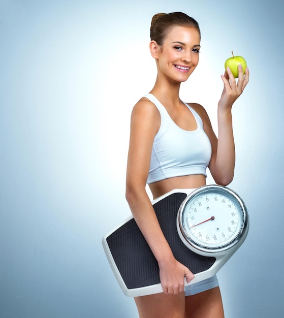 Menos una dieta más un estilo de vida Retrato de una mujer joven consciente de la salud posando con una manzana y una escala en el estudio