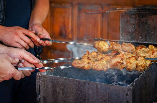 Mens mãos segurando espetos com a carne frita no carvão.