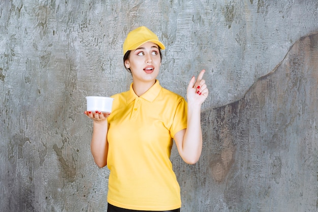 Mensageira de uniforme amarelo segurando uma xícara para levar e apontando para alguém