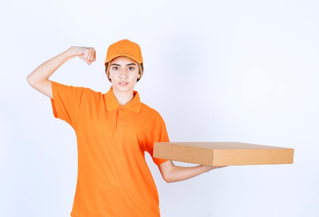 Mensageira de uniforme laranja entregando uma caixa de papelão e mostrando sinal de satisfação