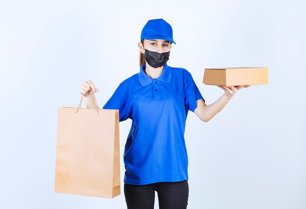 Mensageira feminina com máscara e uniforme azul segurando uma sacola de papelão e uma caixa