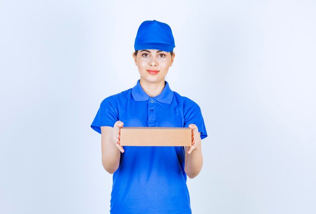 Mensageiro feminino jovem em uniforme azul, dando a caixa de papelão em fundo branco.