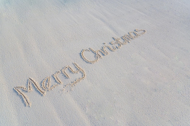 Mensagem de feliz natal manuscrita em areia lisa na costa de uma praia tropical. Sinal natural