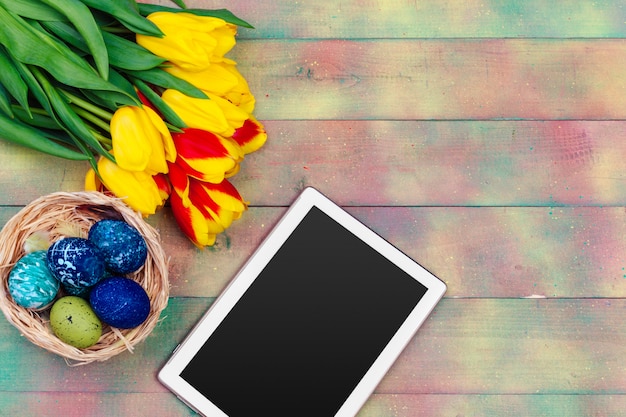 Mensagem na tela do tablet e tulipas coloridas e ovos de Páscoa na madeira
