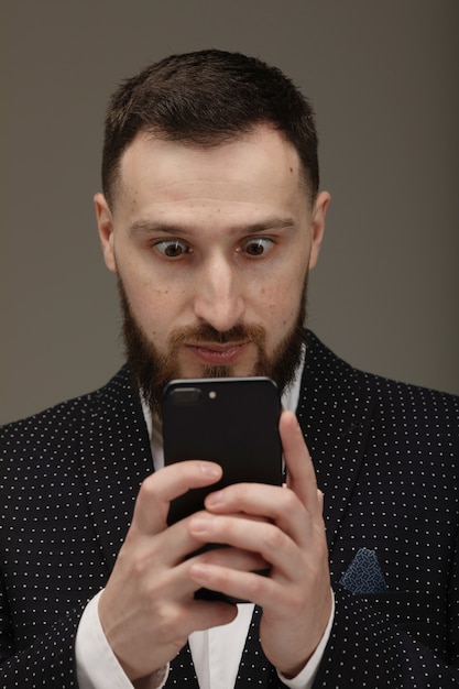 Mensagem texting do homem novo no telefone esperto isolado no fundo cinzento.