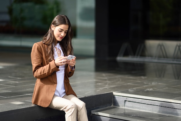 Mensagens de empresária com um smartphone ao lado de um prédio de escritórios