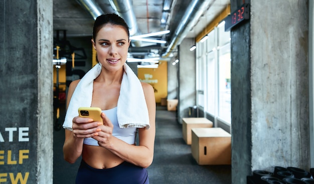 Mensagens de texto sms jovem focada em fitness mulher em roupas esportivas segurando seu smartphone e olhando para o lado enquanto