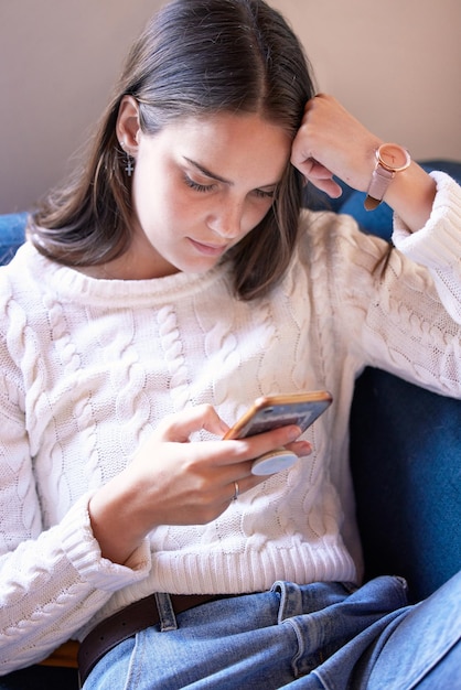 Este mensaje es tan preocupante Foto de una mujer joven sentada en su sofá usando su teléfono inteligente