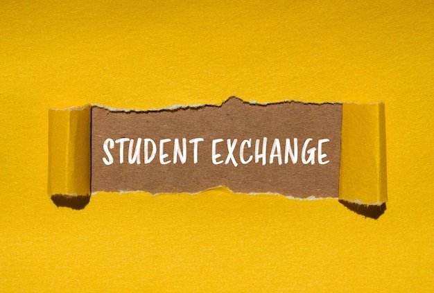Mensaje de intercambio estudiantil escrito en papel amarillo rasgado con fondo marrón Símbolo conceptual de intercambio de estudiantes Copiar espacio