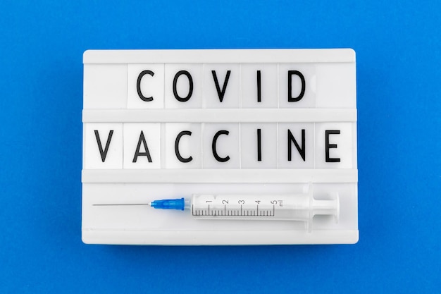 Mensaje de texto de coronavirus de la vacuna covid, primer plano de la inscripción, caja de luz con letras y jeringa médica, vista superior y foto plana