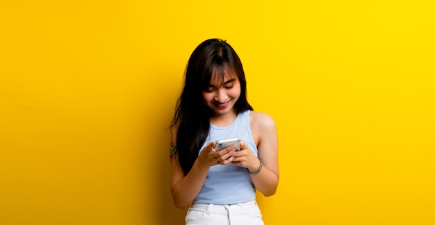 Mensajería de noticias y comunicación en línea Foto de una hermosa mujer asiática linda alegre hablando por teléfono celular aislado sobre fondo de pared amarilla