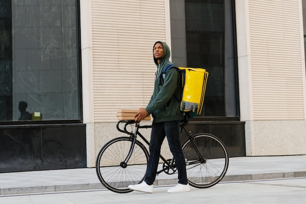 Un mensajero afroamericano en bicicleta Un hombre sostiene cajas de pizza afuera