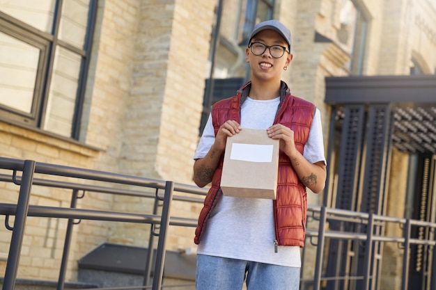 Mensajero asiático joven que sostiene la bolsa de papel pequeña con el espacio de la copia para