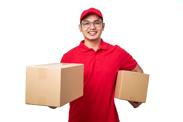 Mensajero asiático sonriente con uniforme rojo sosteniendo dos cajas con pedidos empaquetando artículos de envío para los clientes