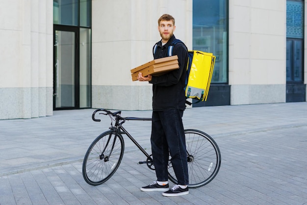 Un mensajero en bicicleta recorre el patio de la casa con cajas de pizza para pasar el pedido al cliente Entrega rápida y ecológica