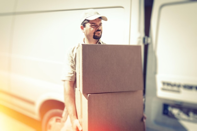 Foto el mensajero con una caja de cartón de pie contra el camión durante un día soleado