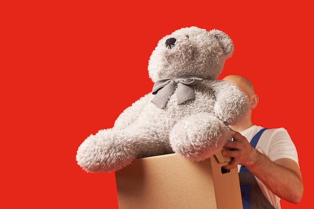 Foto el mensajero calvo lleva una caja de cartón y un oso de peluche encima