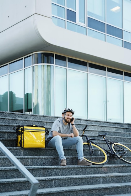 Mensajero de entrega de alimentos exprés sentado en las escaleras con bolsa aislada y bicicleta