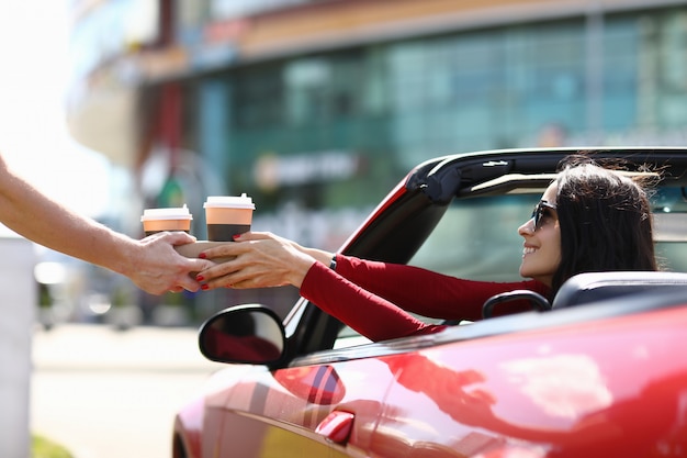 El mensajero entrega el café a la mujer en primer del coche