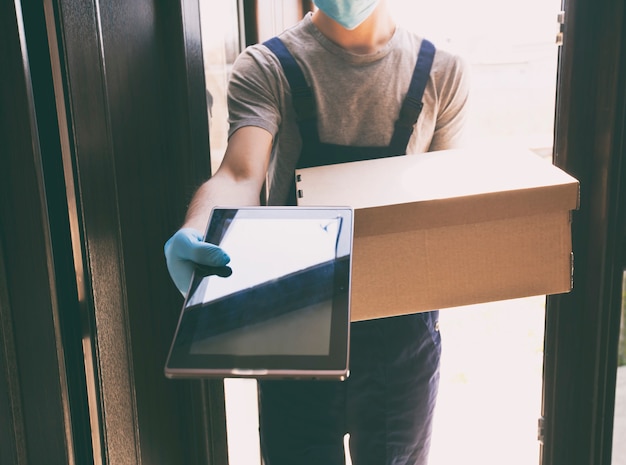 El mensajero entrega la caja de cartón a casa con guantes de látex y mascarilla médica.