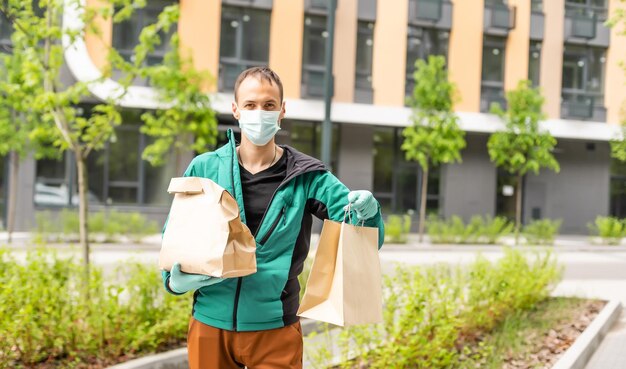 Mensajero de entrega postal con mascarilla protectora frente a la camioneta de carga que entrega la caja de retención del paquete debido a la enfermedad de Coronavirus o COVID-19.