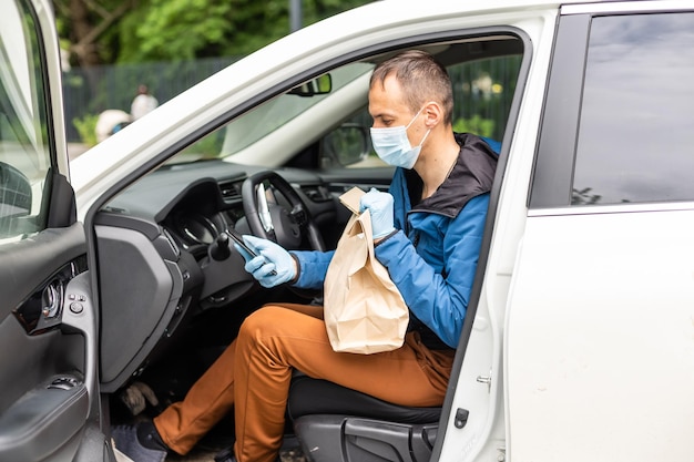 Mensajero de entrega postal con mascarilla protectora frente a la camioneta de carga que entrega la caja de retención del paquete debido a la enfermedad de Coronavirus o COVID-19.