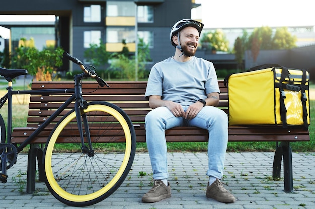 Mensajero de entrega urgente sentado en un banco con bolsa aislada y bicicleta