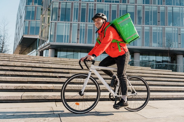 Un mensajero es un hombre con una bolsa termo que entrega comida al cliente de la oficina en una ciudad en bicicleta.