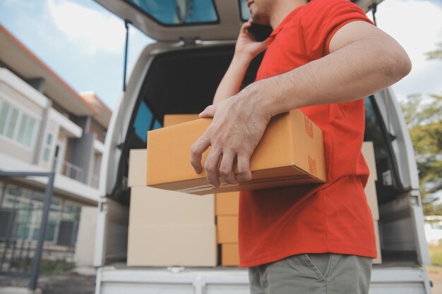 El mensajero expreso asiático joven usa para dar cajas a la mujer cliente que lleva máscara de protección facial en la parte delantera de la casa