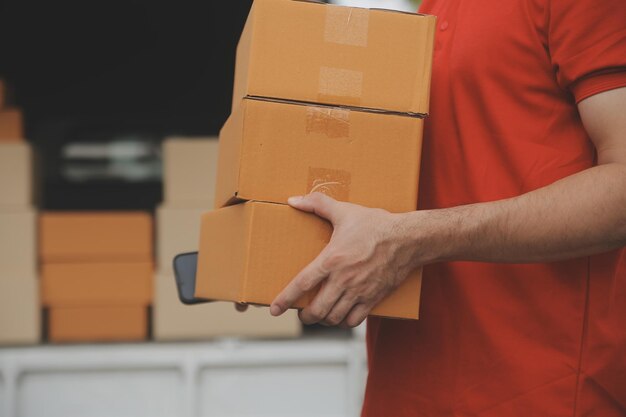 El mensajero expreso asiático joven usa para dar cajas a la mujer cliente que lleva máscara de protección facial en la parte delantera de la casa