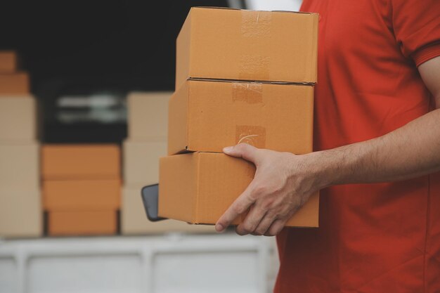 El mensajero expreso asiático joven usa para dar cajas a la mujer cliente que lleva máscara de protección facial en la parte delantera de la casa