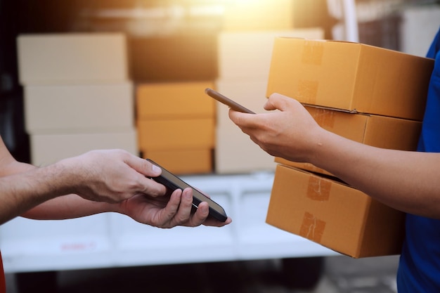 El mensajero expreso asiático joven usa para dar cajas a la mujer cliente que lleva máscara de protección facial en la parte delantera de la casa