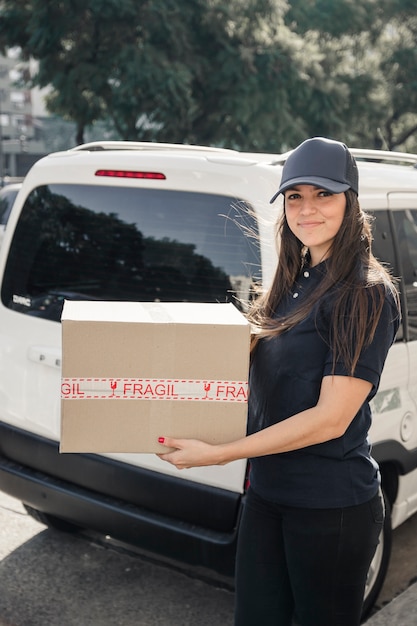 Foto mensajero femenino sonriente con el paquete que se coloca delante o vehículo