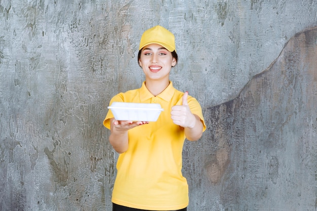 Mensajero femenino en uniforme amarillo entregando una caja de comida para llevar blanca y disfrutando de la comida