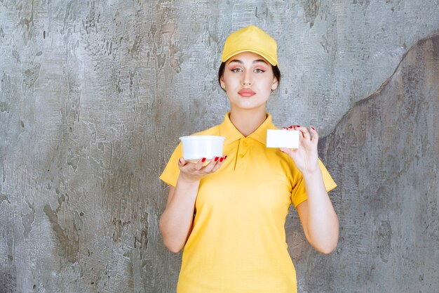 Mensajero femenino en uniforme amarillo sosteniendo una taza de comida para llevar y presentando su tarjeta de visita