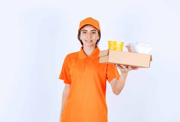 Mensajero femenino en uniforme naranja con cajas de comida para llevar amarillas y blancas