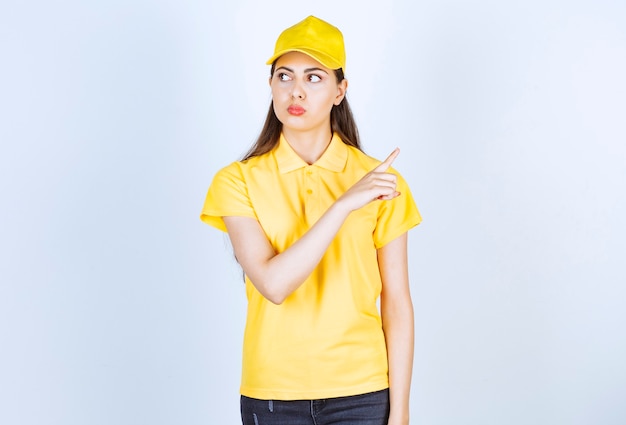 Mensajero de hermosa mujer en uniforme amarillo de pie y posando sobre la pared blanca.